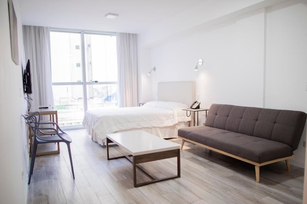A modern hotel room with a bed, sofa, desk, and chair.
