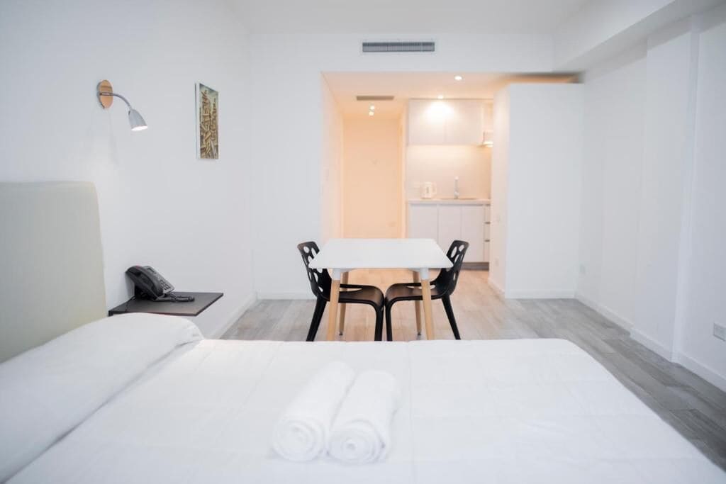 A hotel room with a bed, a desk, a chair, a phone, and a small table.