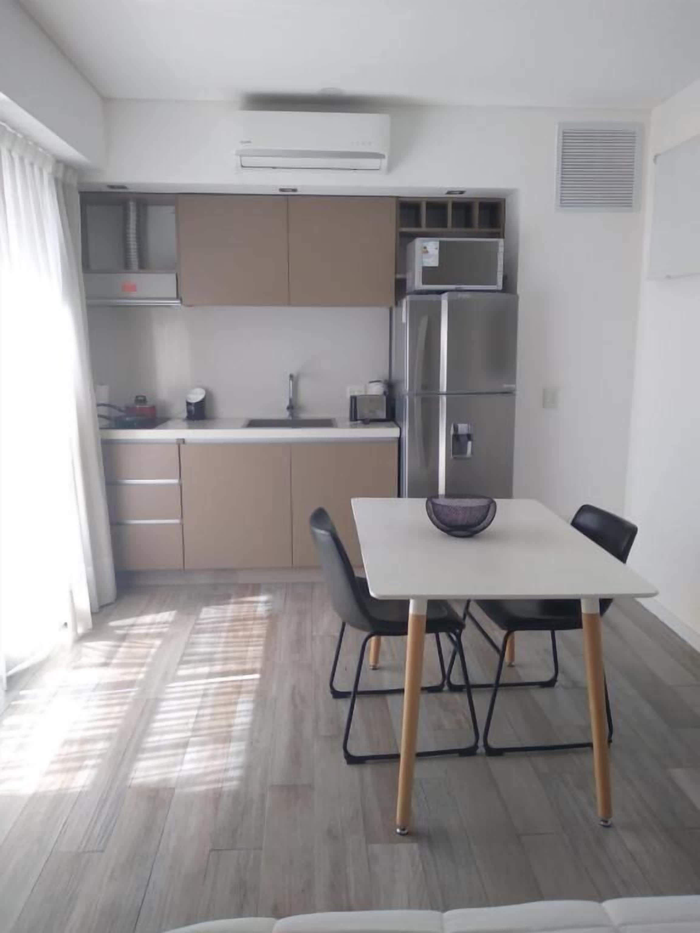 Una cocina moderna con refrigerador, microondas y comedor con mesa y sillas.