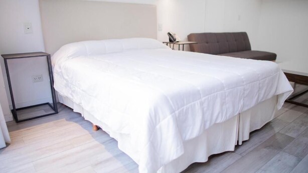 Una habitación de hotel con una cama grande, una mesita pequeña, una silla y una mesita de noche.