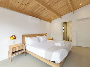 Ein Schlafzimmer mit Holzboden, einem Bett mit weißer Bettwäsche, einem Nachttisch und einer Wandlampe.
