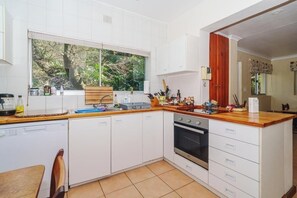 Eine Küche mit weißen Schränken, einer Holz Arbeitsplatte, einem eingebauten Backofen und einem Fenster mit Blick auf Bäume.