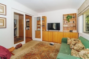 Ein Wohnzimmer mit einem grünen Sofa, einem Flachbildfernseher, Holzschränken und einem gemusterten Teppich.