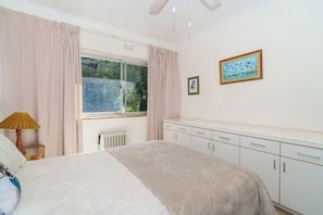 Ein Schlafzimmer mit einem Bett, einem Heizkörper, einem Fenster mit Vorhängen, einer Nachttischlampe und einem Schrank.