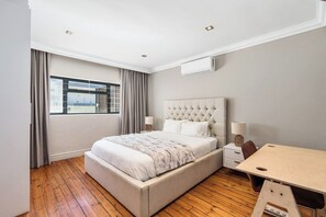 A modern bedroom with a large bed, bedside tables, a desk, and a window with curtains. - Sea Point Gem with Private Pool & Fireplace (Cape Town)