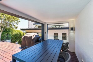 An outdoor patio with a wooden table and chairs, a barbecue grill, and a view of a modern building. - Sea Point Gem with Private Pool & Fireplace (Cape Town)