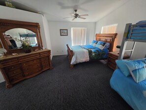 A bedroom with a wooden dresser, a bed with blue bedding, a bunk bed, a ceiling fan, and a window with blinds. - Parker Strip House Riverfront, Dock, Patio & view!  2-bedroom house with AC/ SPA (Parker)