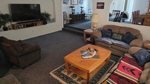 A living room with a flat-screen TV, a wooden coffee table, a brown sofa, and a patterned rug. - Parker Strip House Riverfront, Dock, Patio & view!  2-bedroom house with AC/ SPA (Parker)