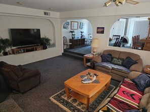 Ein Wohnzimmer mit Flachbildfernseher, Couchtisch aus Holz, braunem Sofa und einem gemusterten Teppich.