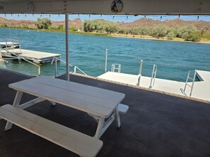 An outdoor picnic table with a view of a calm lake and distant hills. - Parker Strip House Riverfront, Dock, Patio & view!  2-bedroom house with AC/ SPA (Parker)