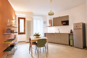 A compact kitchen with a dining area, a microwave, a refrigerator, and a clock on the wall. - Stylish Milan Apartment near M4 & Navigli (Milano)