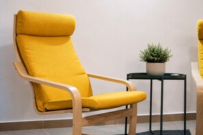 A yellow cushioned chair with wooden armrests, positioned next to a small table with a potted plant. - Stylish Milan Apartment near M4 & Navigli (Milano)