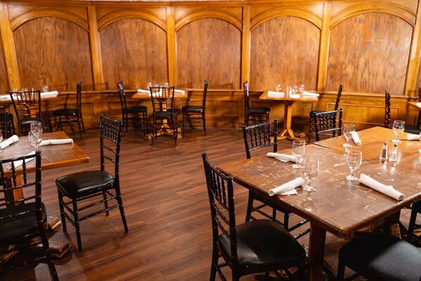Ein Restaurant mit Holzwandverkleidung, Tischen gedeckt mit Gläsern und Servietten und Stühlen darum herum.