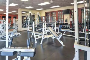 Ein Fitnessstudio mit verschiedenen Gewichtsmaschinen, Spiegeln und einem Fernseher an der Wand.