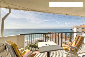 Ein Balkon mit Meerblick, einem Tisch und gestreiften Stühlen.