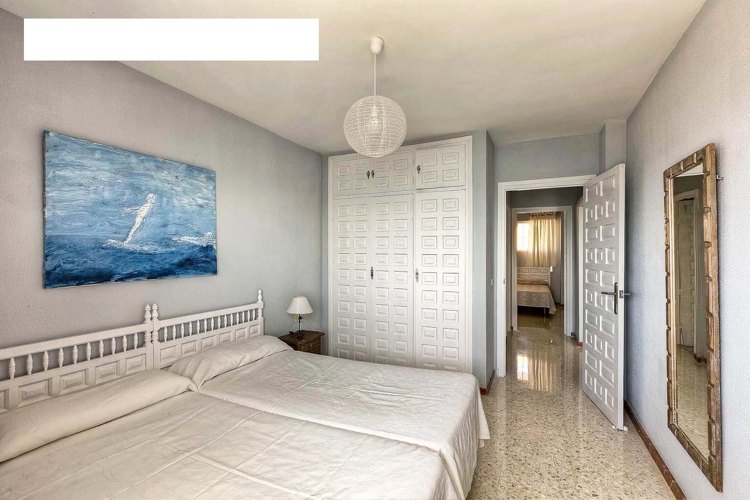 Een slaapkamer met een groot bed, een schilderij van een zeilboot, een kledingkast en een gang naar een andere kamer.