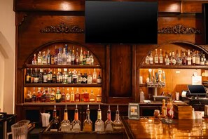 Eine Bar mit Regalen voller Spirituosenflaschen, einem darüber hängenden Fernseher und einer Theke mit Registrierkasse und Laptop.