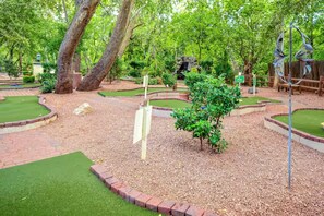 Ein Minigolfplatz mit grünen Spielbahnen, Sandfällen und einer Holzbrücke.