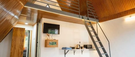 A modern interior with a wooden sloped ceiling, a built-in TV, and a kitchen area with a microwave and kettle.