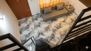 Un interior moderno con piso de mármol, un sofá, una mesita con una planta y una escalera.