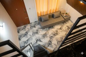 A modern interior with a marble floor, a sofa, a small table with a plant, and a staircase.