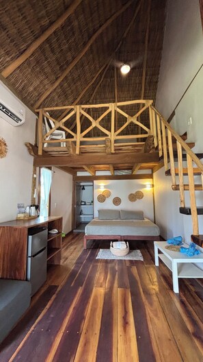 Un interior rústico con un dormitorio en entrepiso, una escalera de madera y una kitchenette.