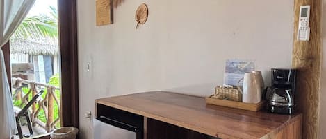 A compact kitchen with a refrigerator, a coffee maker, and a wooden counter.
