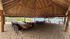A beachside hut with a thatched roof, wooden tables, and chairs, overlooking the sea.