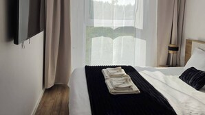 A hotel room with a bed, a flat-screen TV mounted on the wall, a window with curtains, and a ceiling light fixture.