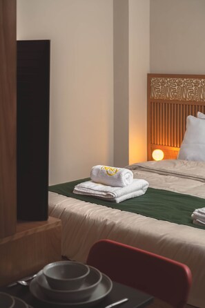 A hotel room with a neatly made bed, a green bedspread, a white pillow, and a wall-mounted TV. - Solé ORO Rooftop Studio I Nesty Hospitality (Al Maadi)