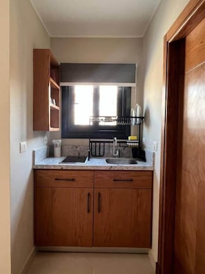 A compact kitchen with wooden cabinets, a countertop, and a window above the sink.