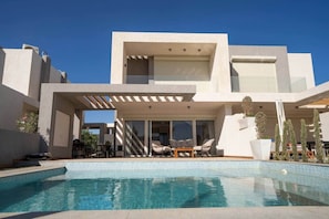 Un bâtiment moderne à deux étages, doté d’une piscine, d’un espace extérieur aménagé et d’une pergola.