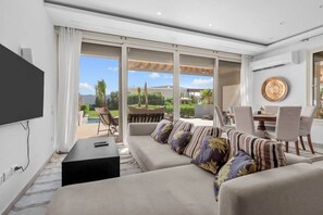 A modern living room with a sofa, a coffee table, and a TV. There is a dining area with chairs and a table. The room has large windows and a view of the outdoors. - Casa Maraya with private pool I Nesty Hospitality (Second Hurghada)