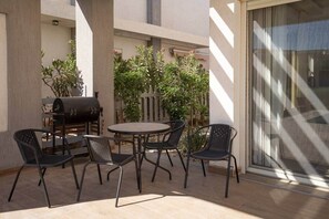 Eine Außenpatio mit einem runden Tisch, vier Stühlen, einem Grill und einem Blumentopf.