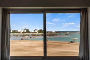 Blick durch ein Fenster auf Strand und Wasserlandschaft im Hintergrund.
