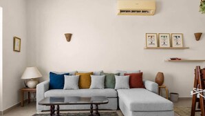 A living room with a grey sectional sofa, a coffee table, a lamp, a rug, an air conditioner, wall-mounted lights, framed artwork, and a bookshelf. - The Sandy Feet. Part II - Nesty Hospitality (Hurghada)