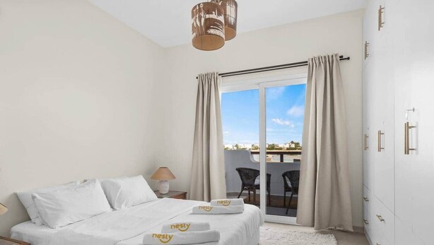 A hotel room with a bed, a nightstand, a lamp, a view of the outside, and a balcony with chairs. - The Sandy Feet. Part II - Nesty Hospitality (Hurghada)