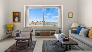 A living room with a view of the beach, a sofa, a chair, a coffee table, and a lamp. - The Sandy Feet. Part II - Nesty Hospitality (Hurghada)
