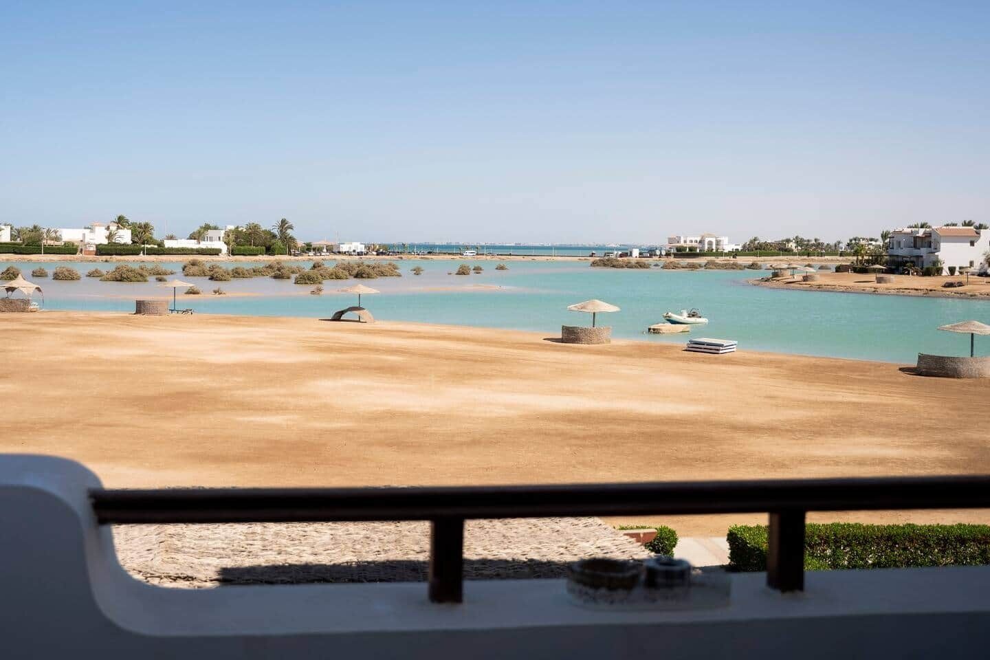 A coastal view with a sandy beach, clear blue water, and a few umbrellas.
