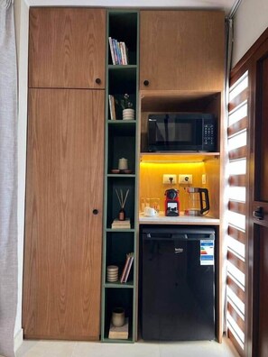 Eine kompakte Küchenzeile mit Mikrowelle, Kaffeemaschine und kleinem Kühlschrank.