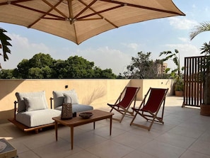 Eine Dachterrasse mit einer Couch, zwei Liegestühlen, einem Tisch und einem großen Sonnenschirm.