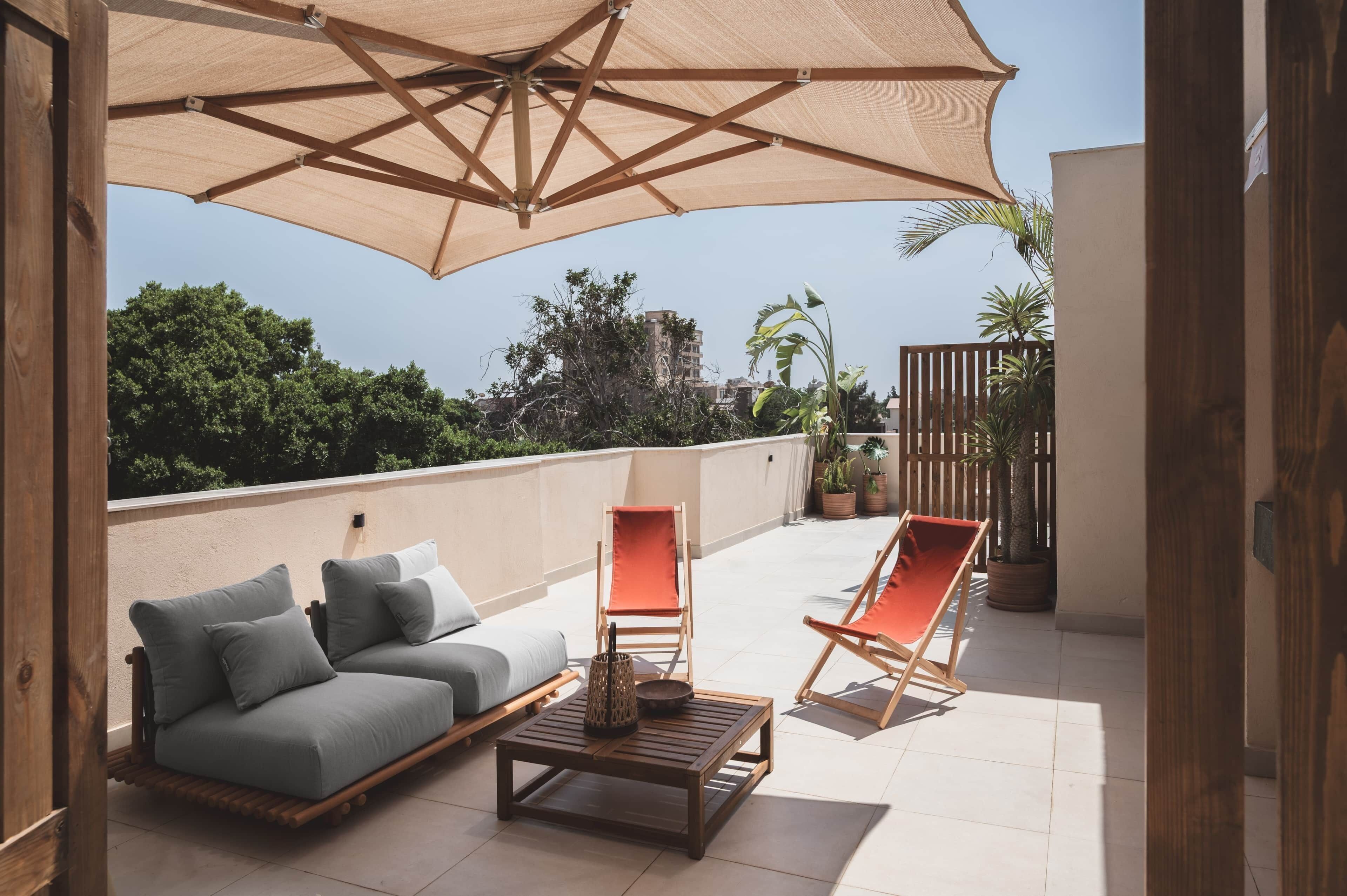 A rooftop terrace with a sofa, two chairs, a table, and a large umbrella providing shade.