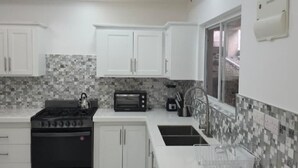 Una cocina moderna con alacenas blancas, estufa a gas, microondas y salpicadero de azulejos.
