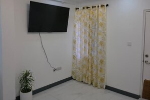A room with a flat-screen TV mounted on the wall, a potted plant, and a floral curtain.
