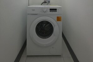 Eine weiße Waschmaschine in einem Raum mit weißen Wänden und einem schwarzen Streifen am Boden.