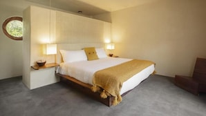 A bedroom with a large bed, bedside lamps, a wooden nightstand, and a circular window. - Angelique s Boutique Spa & Suites (Troncones)