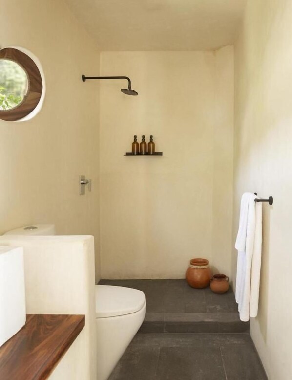 Un baño estrecho con inodoro, ducha y un pequeño estante con botellas.