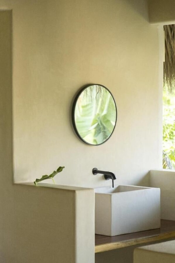 Un baño con lavamanos blanco, un espejo redondo y una planta.
