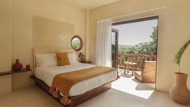 A bedroom with a large bed, a view of a balcony, and a wooden floor. - Angelique s Boutique Spa & Suites (Troncones)