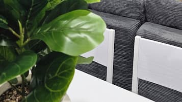 A modern interior with a white table, a potted plant, a grey sofa, and a wall-mounted TV.